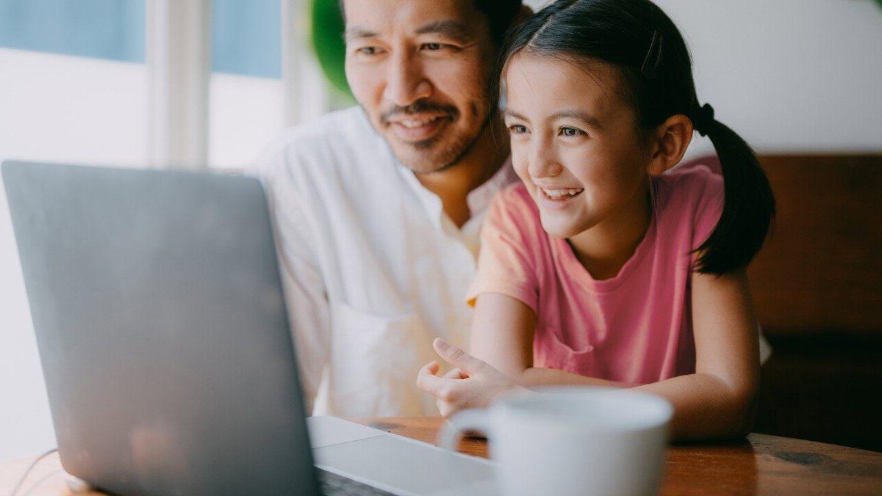 Father and young daughter on video call on laptop at home